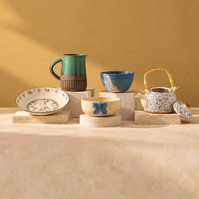 Serveware: a green ceramic jug, a blue bowl, a painted plate, a bow bowl and a blue teapot on stone blocks