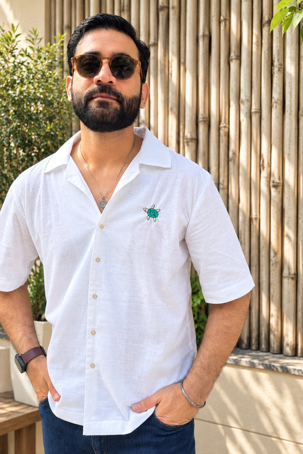 Men: a man in a white short-sleeved shirt and sunglasses in a leafy courtyard