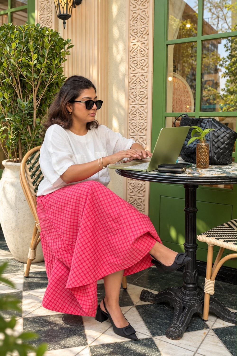 Women: a woman in a white top and pink checked skirt works at a cafe table