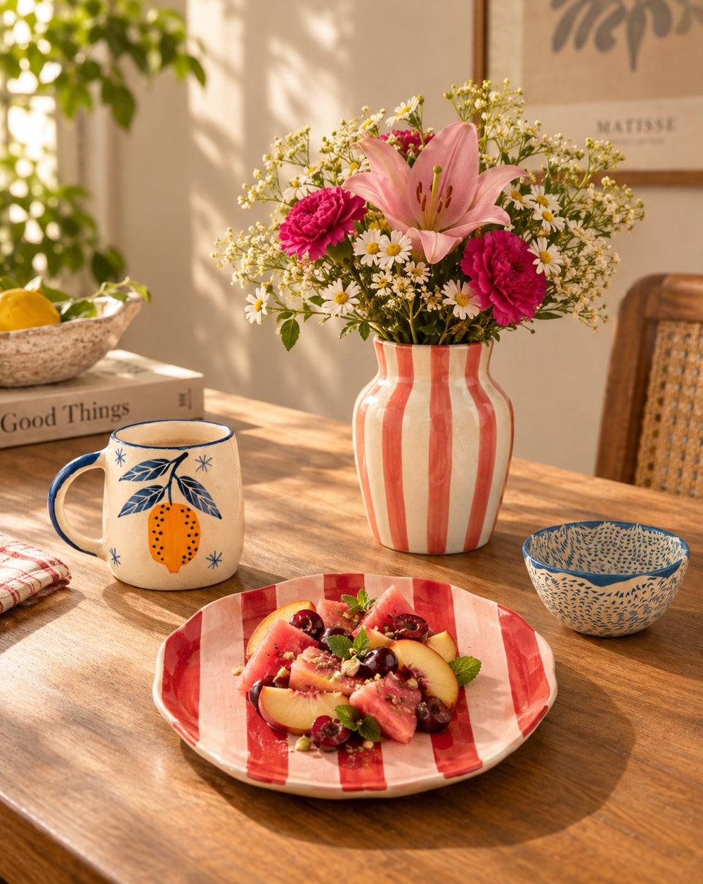 Ceramics: a striped vase of flowers, a painted mug and a striped plate on a wooden table