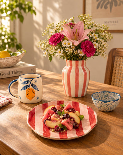 Ceramics: a striped vase of flowers, a painted mug and a striped plate on a wooden table