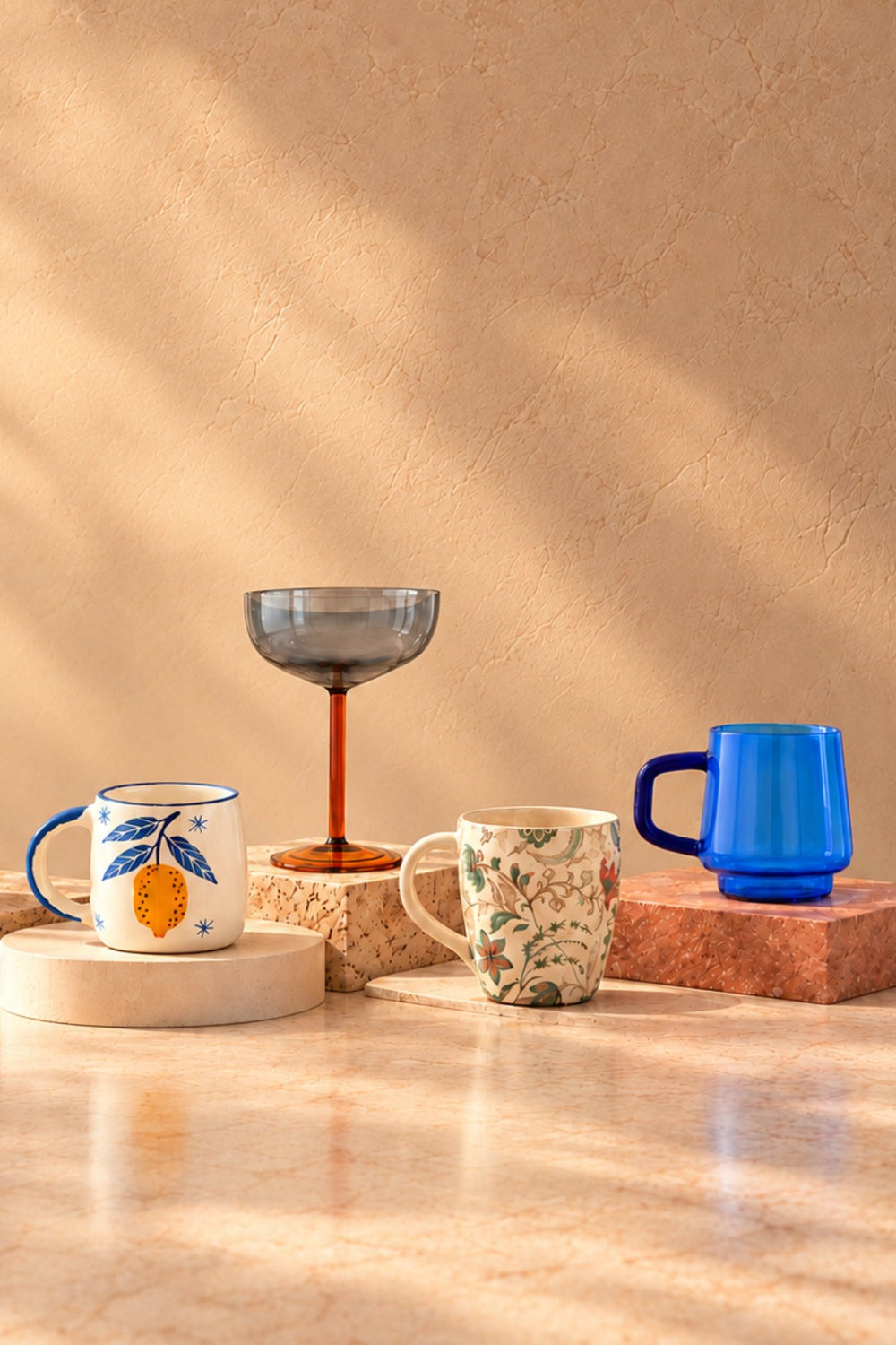 Drinkware: hand-painted ceramic mugs, a blue glass mug and a smoke grey coupe on stone blocks