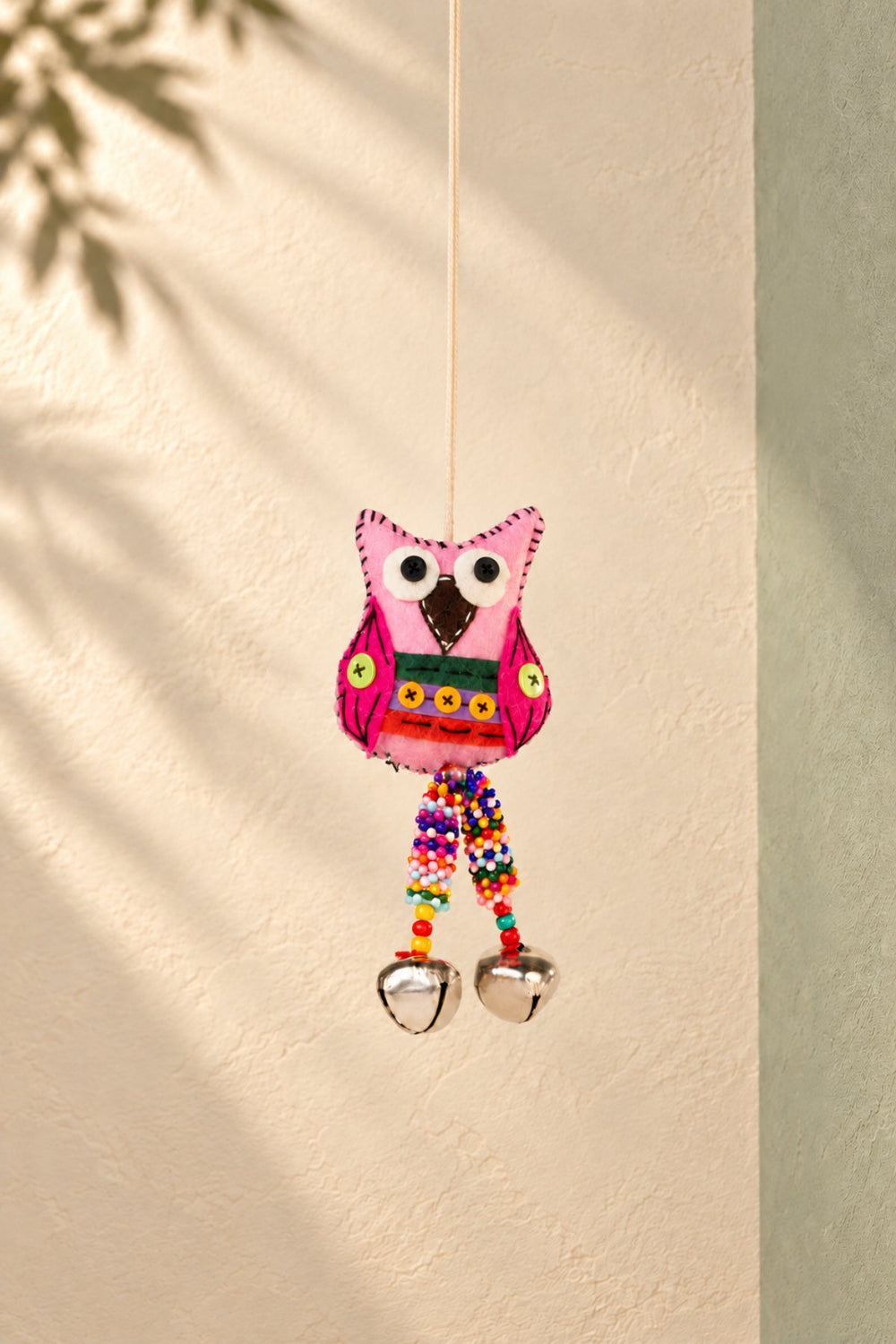 Hanging decorations: a pink embroidered wool-felt owl with bells hanging against a sunlit wall