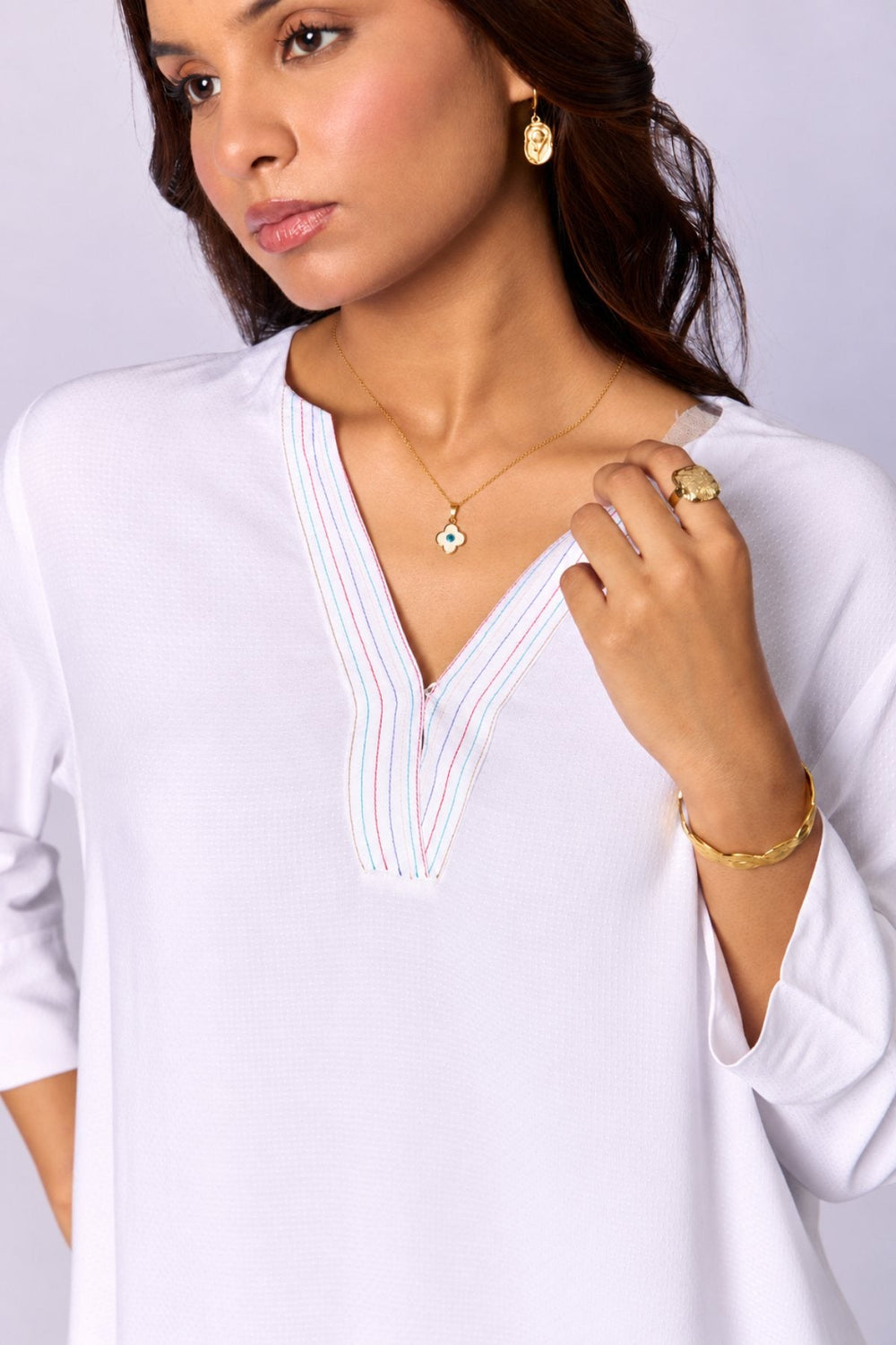 Jewellery: a woman in a white tunic wearing gold-toned earrings, a pendant and rings