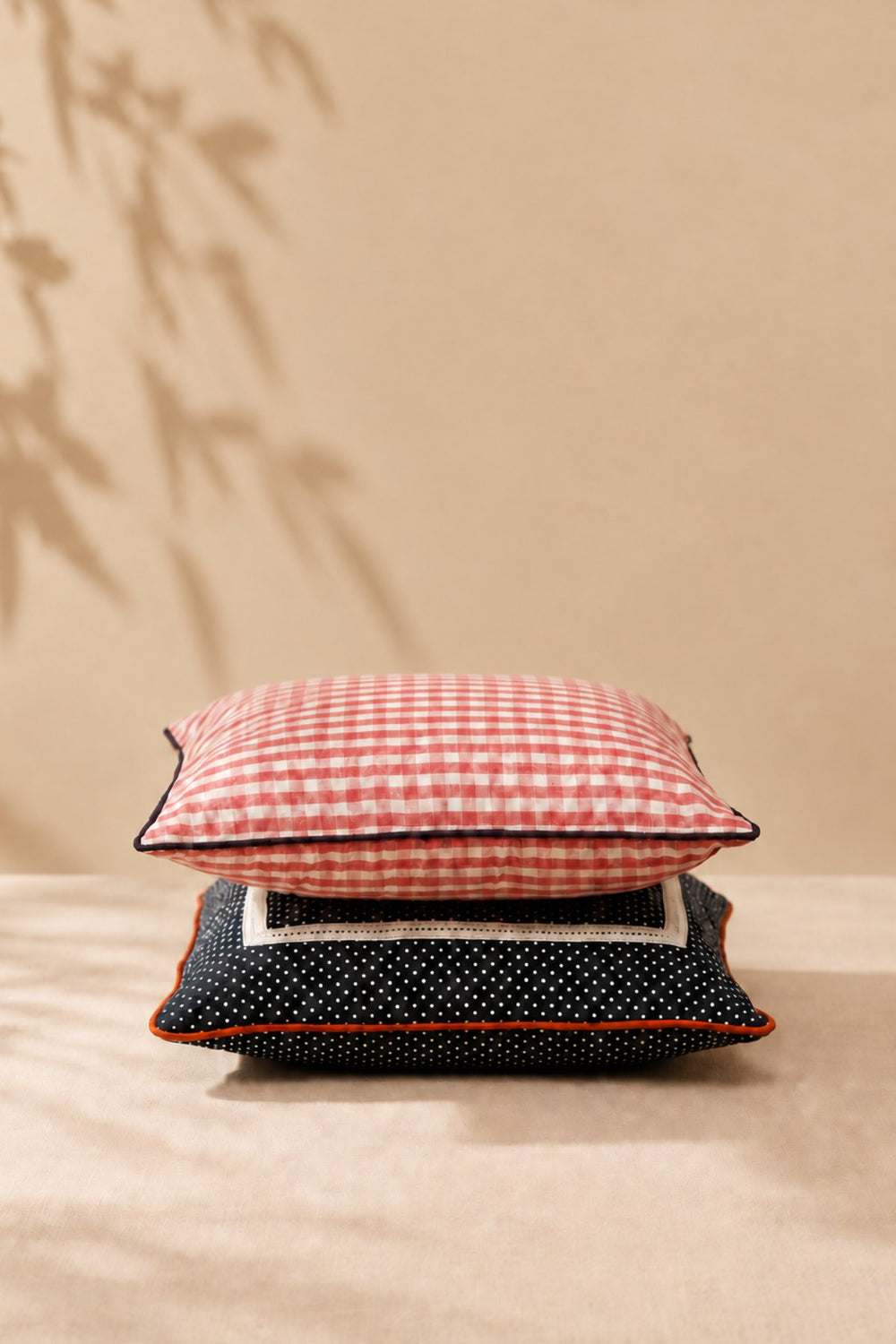 Set of two cushion covers: a pink gingham cover stacked on a charcoal dotted cover