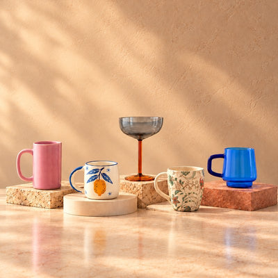 Drinkware: ceramic mugs, a blue glass mug and a coupe on stone blocks